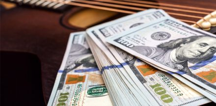 How to Make Money with Music - Dollar bills on acoustic guitar. Close up.