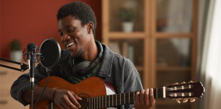 "How To Record Vocals at Home" Portrait of talented African-American man singing to microphone and playing guitar while recording music.