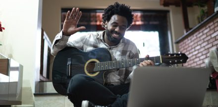 "How Musicians Make Money as Indie Artists" - Acoustic guitar teaching through a video call, waving to laptop