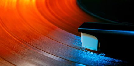 "What Are Vinyl Records Made Of?" - Close up photo of analog music player playing on turntable with needle illuminated in warm, cozy sunset light. Concept of art, retro music, vintage, disco, nostalgy, old-fashion.